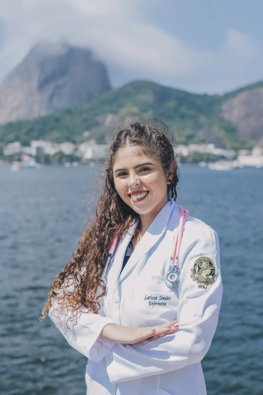 Larissa Simões, enfermeira, sorrindo de jaleco branco com estetoscópio rosa